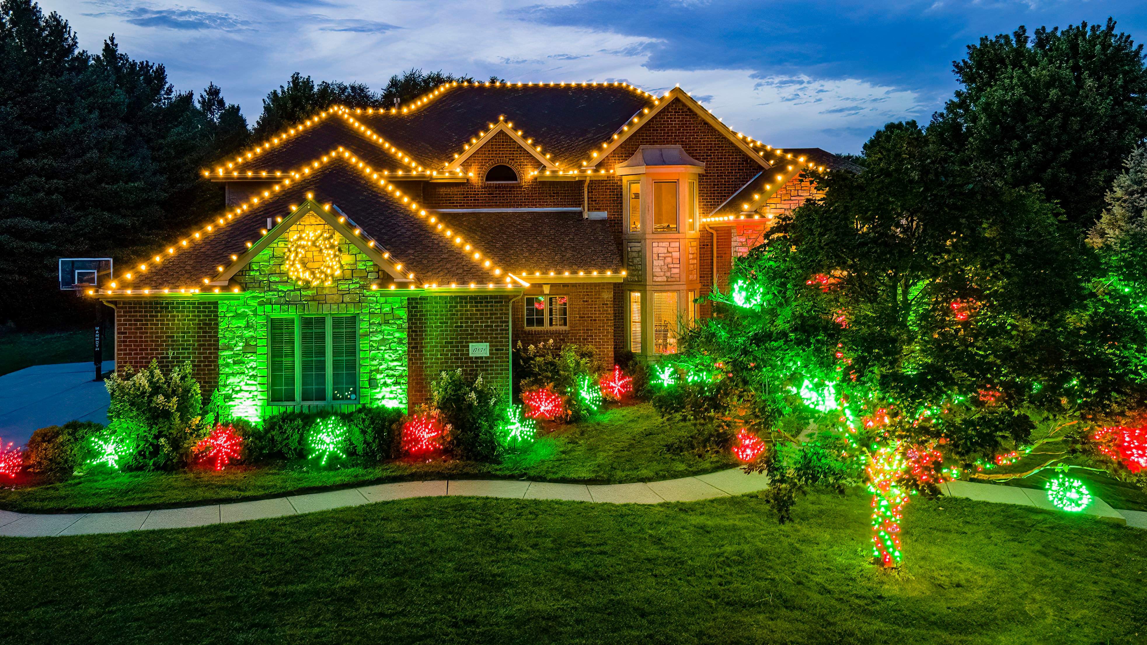 Home with warm roofline lights and red and green lights on shrubs and trees