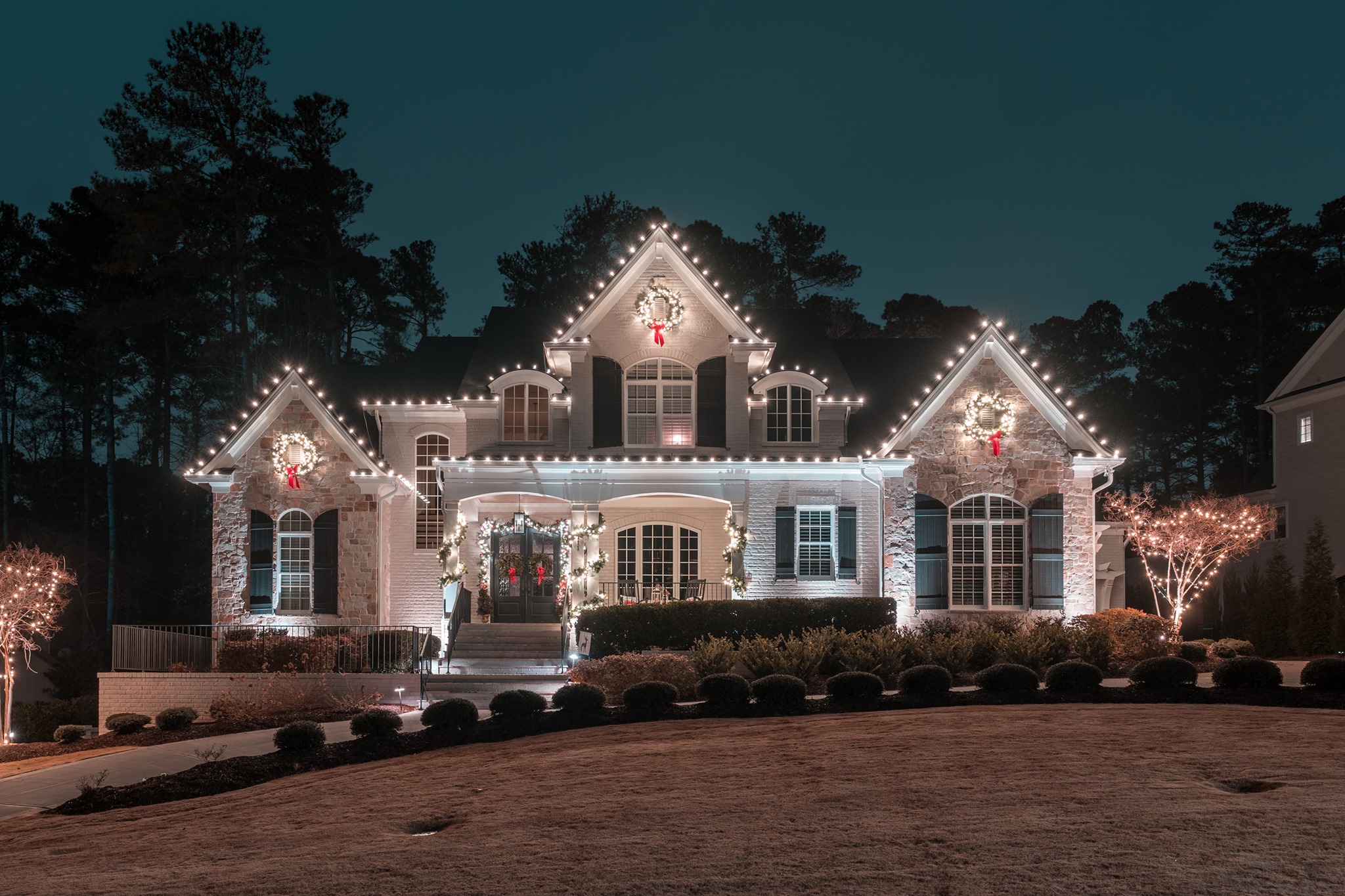 Home decorated with white roofline lights, wreaths and illuminated trees